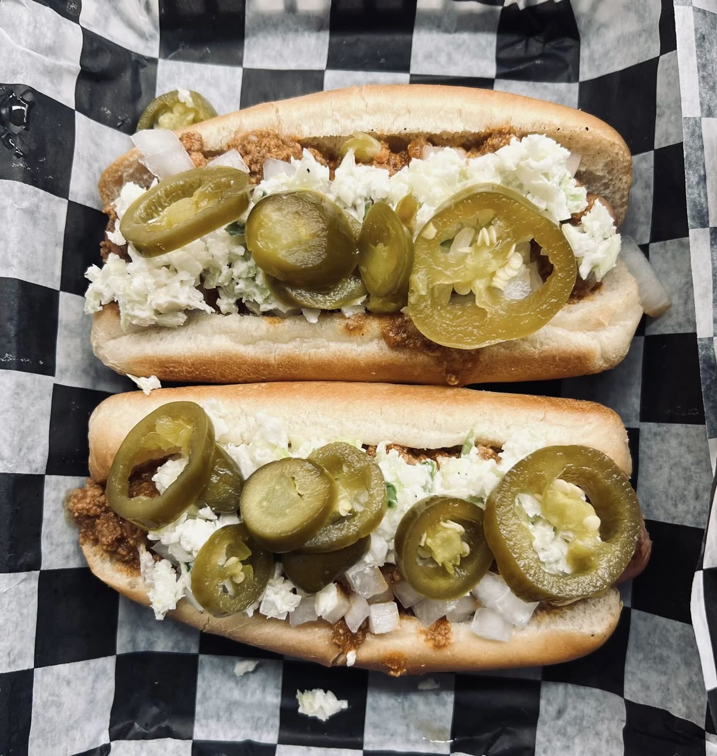 Two slaw dogs stacked with jalapenos in a checkered basket