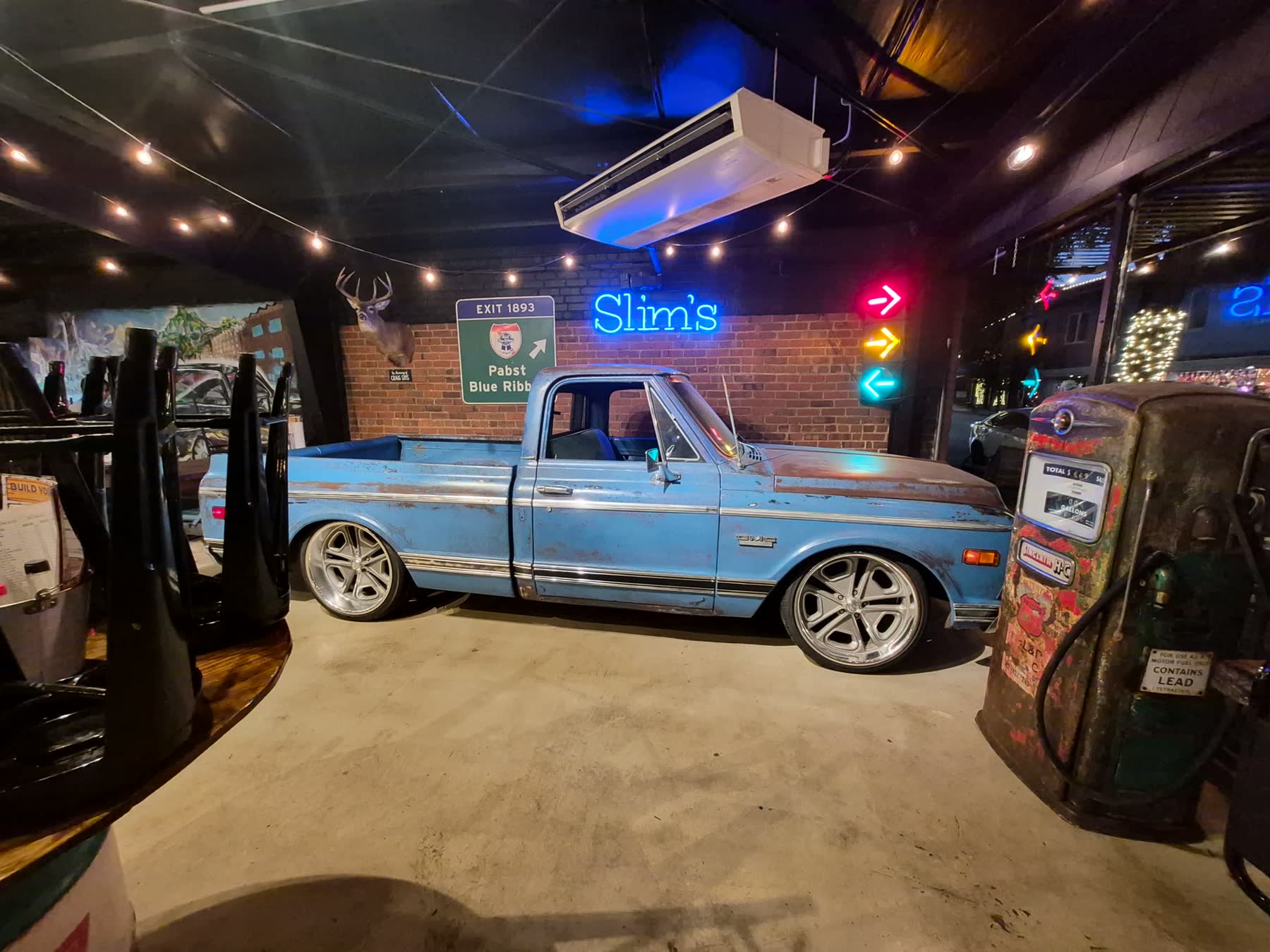 The patina GMC parked inside Slim's at night, the blue Slim's neon and arrow signs glowing over the bar